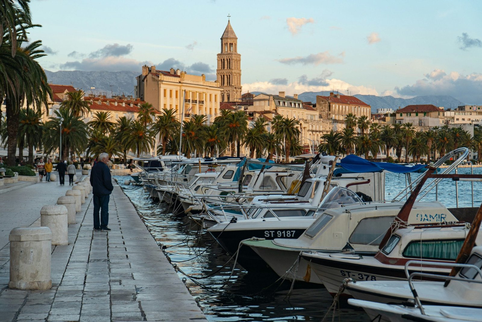 man in black jacket walking on dock near white and blue boats during daytime